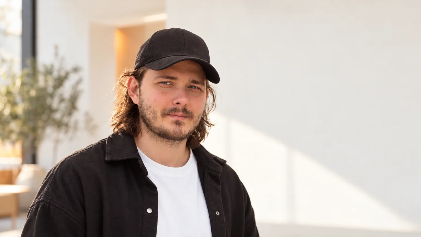 Portrait of the person behind Zafeiry, wearing a black cap and overshirt in a bright interior.